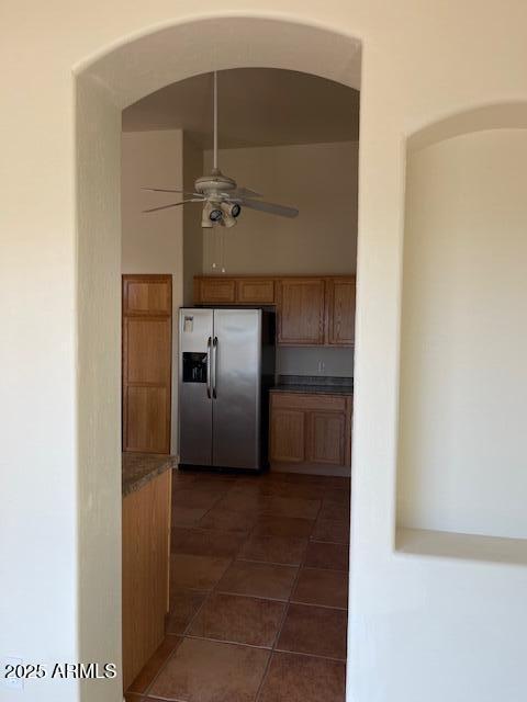 kitchen featuring stainless steel fridge with ice dispenser, arched walkways, ceiling fan, dark tile patterned floors, and brown cabinets