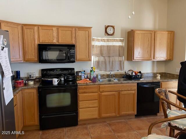 kitchen featuring black appliances, light tile patterned floors, dark stone counters, and sink