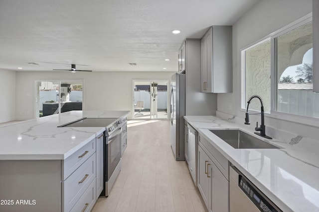 kitchen featuring sink, gray cabinetry, stainless steel appliances, light stone countertops, and a kitchen island