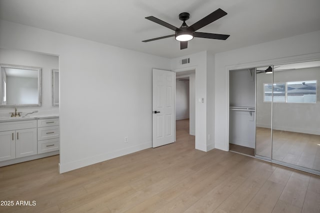 unfurnished bedroom featuring sink, ensuite bath, light wood-type flooring, a closet, and ceiling fan