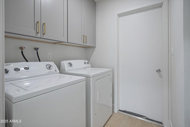 laundry area featuring washing machine and dryer, cabinets, and light wood-type flooring