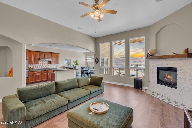 living area with light wood finished floors, baseboards, a ceiling fan, and a stone fireplace