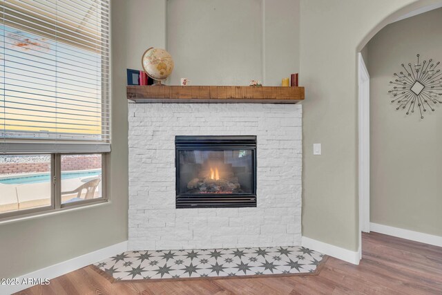 details with a stone fireplace, wood finished floors, baseboards, and arched walkways
