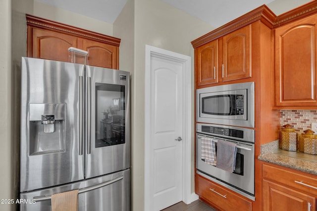 kitchen with appliances with stainless steel finishes, decorative backsplash, brown cabinets, and light stone countertops