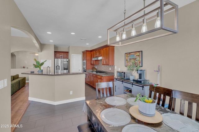 dining area featuring recessed lighting, a toaster, baseboards, dark tile patterned floors, and arched walkways