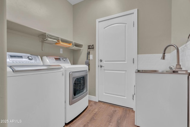 clothes washing area featuring washing machine and dryer, laundry area, light wood-style flooring, and a sink