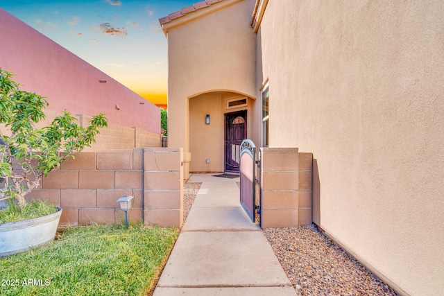 exterior entry at dusk featuring stucco siding, fence, and a gate