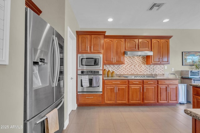 kitchen featuring tasteful backsplash, light stone counters, visible vents, under cabinet range hood, and appliances with stainless steel finishes