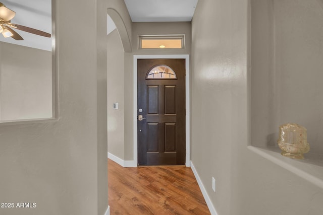 entryway featuring arched walkways, baseboards, a ceiling fan, and wood finished floors