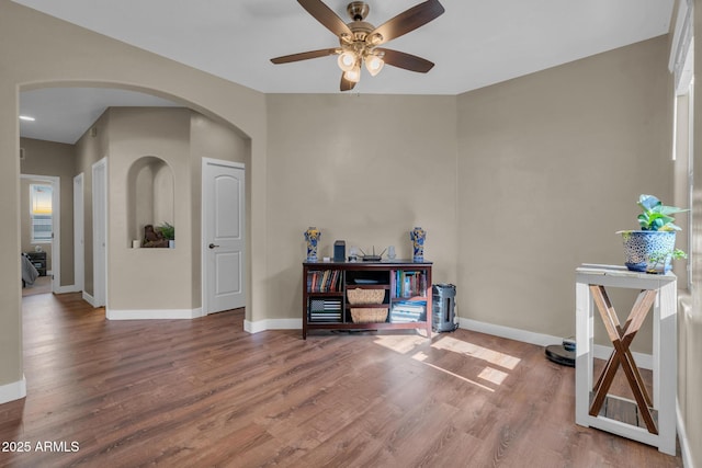 misc room featuring arched walkways, baseboards, a ceiling fan, and wood finished floors