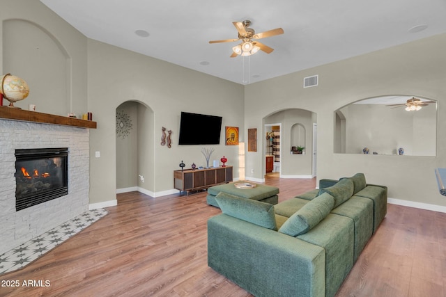 living area featuring wood finished floors, visible vents, ceiling fan, baseboards, and a stone fireplace