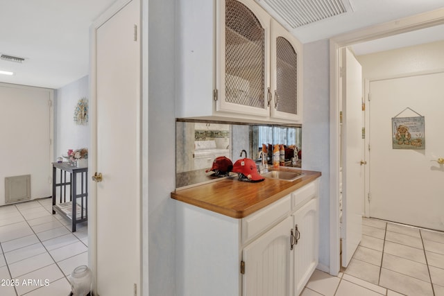 kitchen with light tile patterned flooring, backsplash, sink, and white cabinets