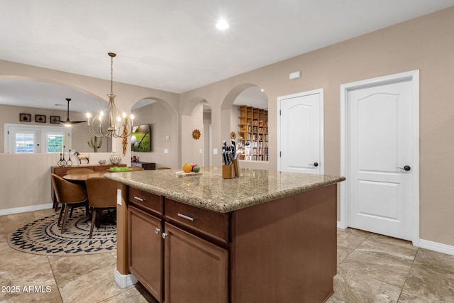 kitchen with light stone counters, a notable chandelier, baseboards, hanging light fixtures, and a center island