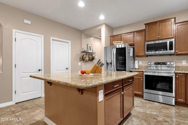 kitchen featuring a breakfast bar, brown cabinets, stainless steel appliances, a kitchen island, and light stone countertops