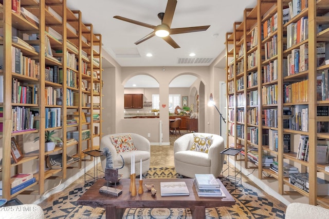 living area featuring arched walkways, recessed lighting, bookshelves, visible vents, and ceiling fan