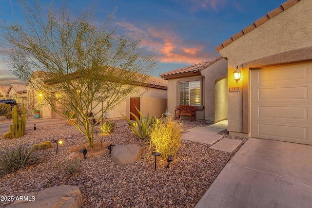 property exterior at dusk with fence, an attached garage, a tile roof, and stucco siding