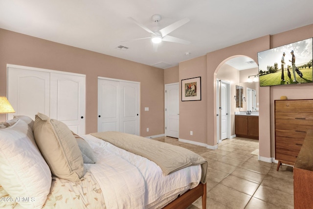 bedroom with arched walkways, visible vents, baseboards, multiple closets, and ensuite bath