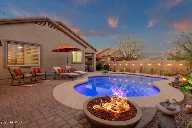 pool at dusk featuring a fenced in pool, an outdoor fire pit, a patio area, and a fenced backyard