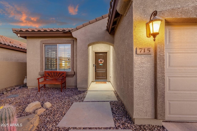 exterior entry at dusk with a garage and stucco siding