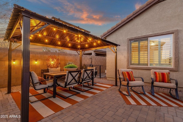 patio terrace at dusk with a gazebo, outdoor dining space, and fence