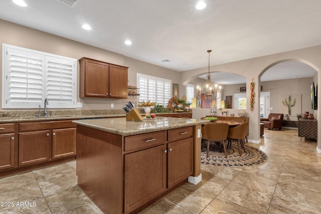 kitchen featuring arched walkways, light stone counters, a sink, a center island, and an inviting chandelier