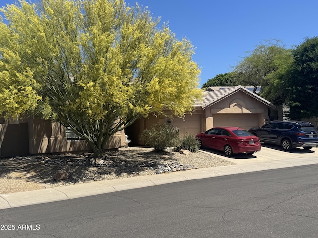 view of property hidden behind natural elements with an attached garage, concrete driveway, and stucco siding