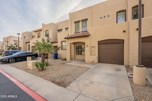 view of front facade with an attached garage, a tile roof, concrete driveway, and stucco siding