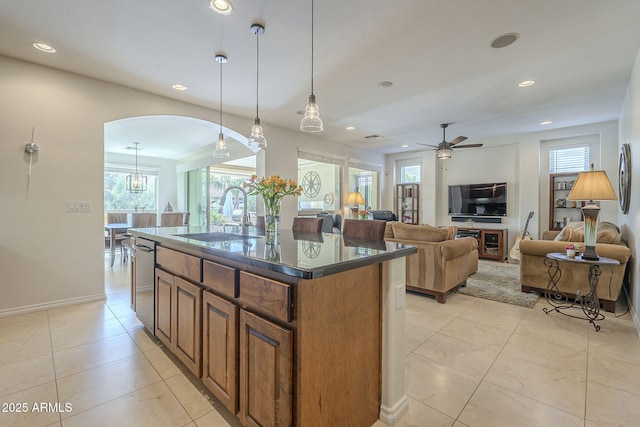 kitchen with a wealth of natural light, brown cabinetry, dark countertops, a sink, and stainless steel dishwasher