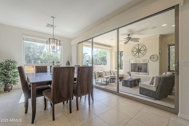 dining space with light tile patterned floors, a premium fireplace, visible vents, and ceiling fan with notable chandelier