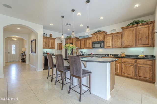 kitchen featuring arched walkways, dark countertops, brown cabinets, a kitchen bar, and black microwave