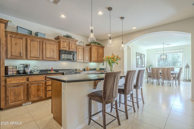 kitchen with dark countertops, a kitchen island, brown cabinets, a kitchen breakfast bar, and black microwave