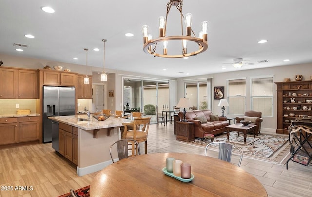 kitchen with ceiling fan with notable chandelier, decorative light fixtures, stainless steel appliances, sink, and light stone counters