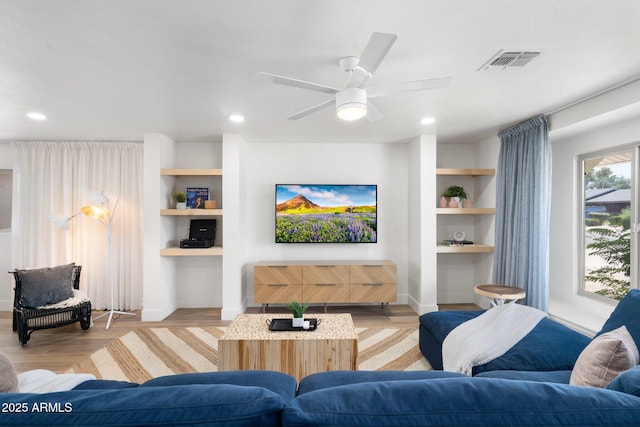 living room with built in features, light hardwood / wood-style floors, and ceiling fan