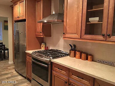 4832 E Cambridge Ave, Phoenix, AZ 85008 - kitchen featuring wall chimney exhaust hood, stainless steel appliances, light countertops, light wood-type flooring, and brown cabinetry
