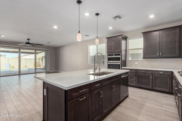 kitchen featuring pendant lighting, sink, decorative backsplash, stainless steel appliances, and a center island with sink