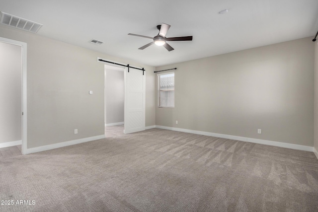 unfurnished bedroom featuring a barn door, light carpet, and ceiling fan