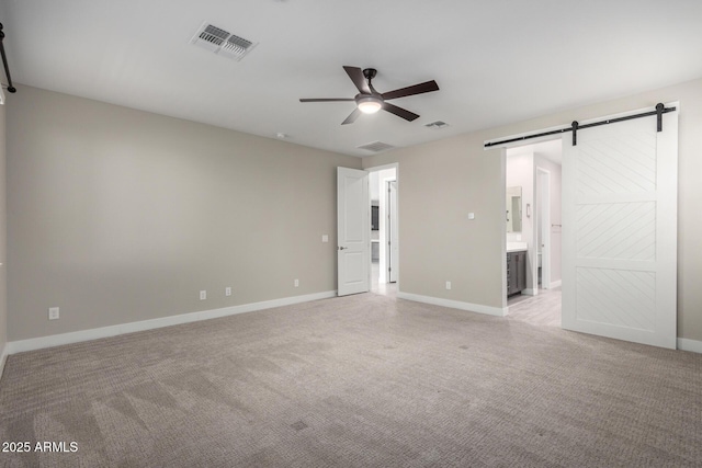 unfurnished room featuring ceiling fan, light colored carpet, and a barn door