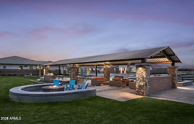 back house at dusk featuring a fire pit, a lawn, and a patio