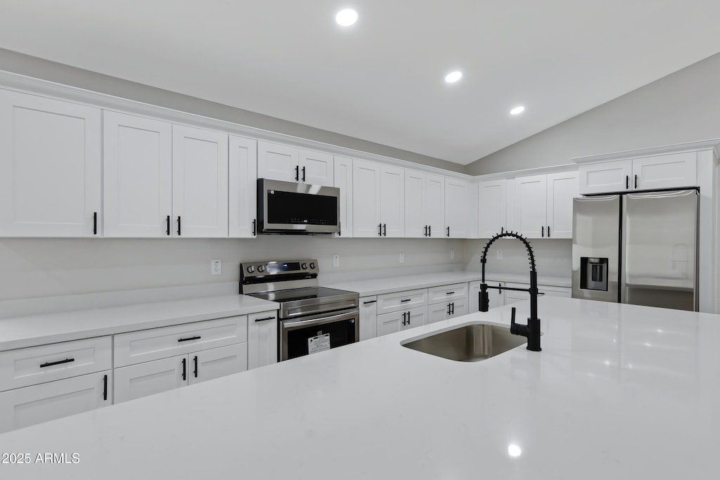 kitchen featuring vaulted ceiling, stainless steel appliances, white cabinets, and sink