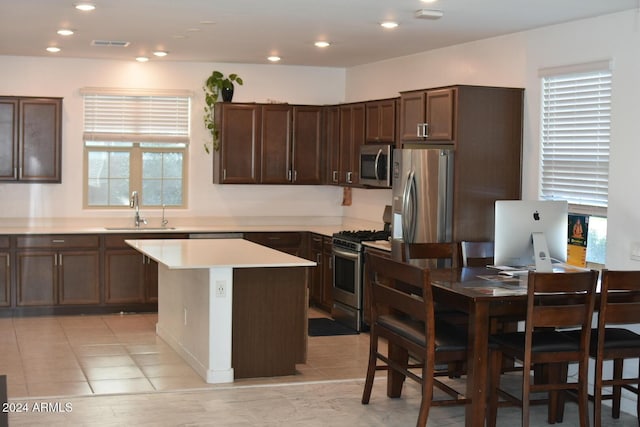 kitchen featuring light tile patterned flooring, dark brown cabinetry, sink, a center island, and appliances with stainless steel finishes