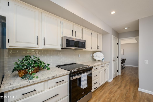 kitchen with baseboards, electric range oven, stainless steel microwave, white cabinetry, and backsplash