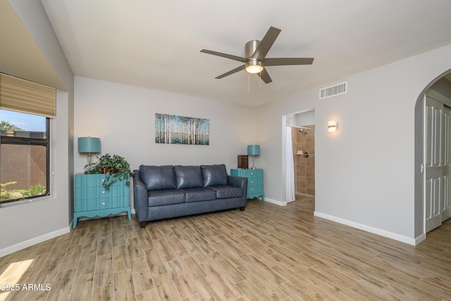 living area with a ceiling fan, visible vents, arched walkways, light wood-type flooring, and baseboards