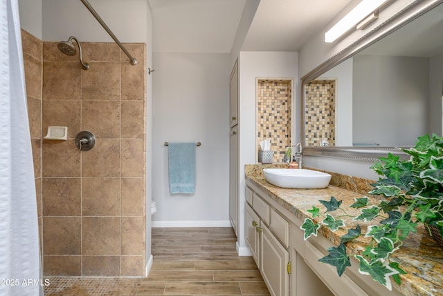 full bathroom with vanity, baseboards, wood finished floors, and tiled shower