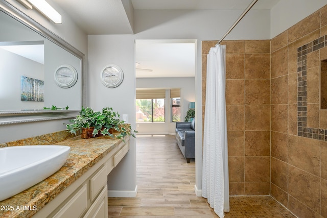 ensuite bathroom with vanity, wood finished floors, baseboards, ensuite bathroom, and tiled shower