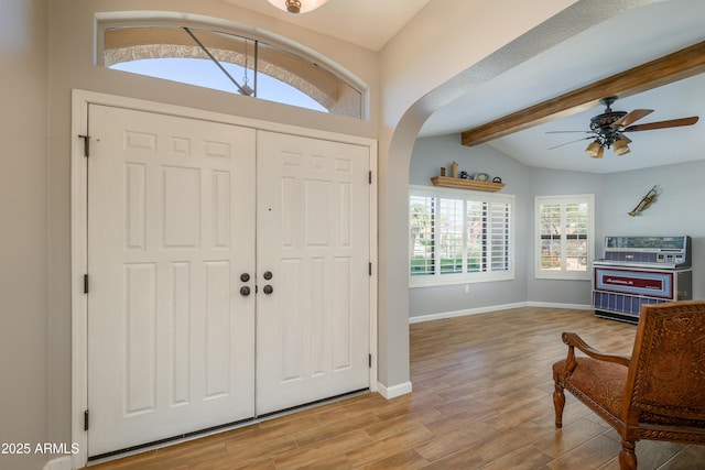 foyer entrance with wood finished floors, baseboards, ceiling fan, arched walkways, and lofted ceiling with beams