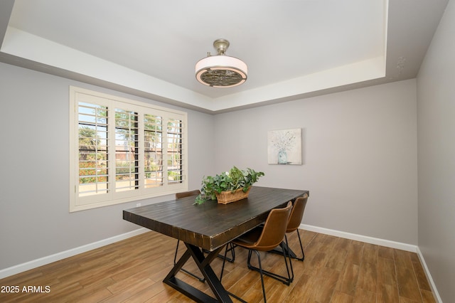 dining space featuring baseboards, a raised ceiling, and light wood-style floors