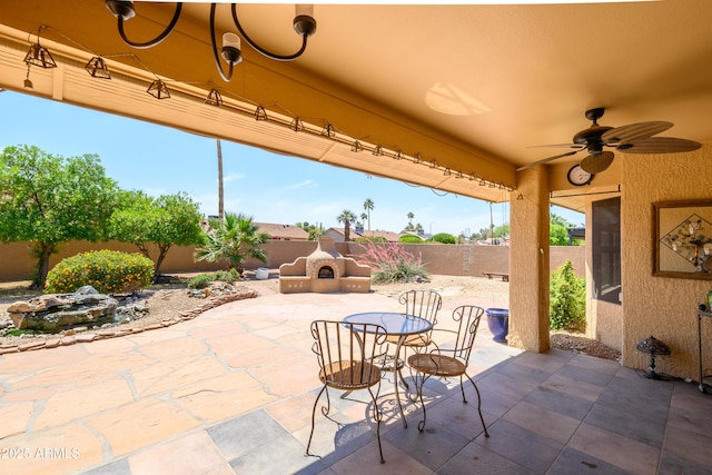 view of patio featuring an outdoor stone fireplace, a fenced backyard, and a ceiling fan