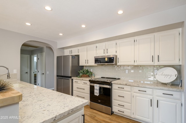 kitchen featuring a sink, arched walkways, stainless steel appliances, and light stone counters