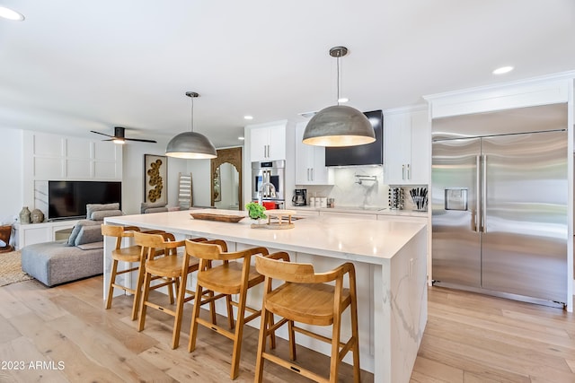 kitchen featuring a breakfast bar, a large island, white cabinetry, hanging light fixtures, and built in fridge