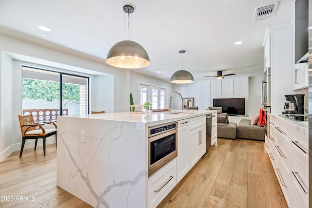 kitchen with white cabinets, pendant lighting, a center island with sink, and ceiling fan